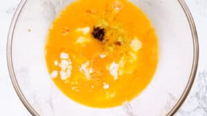 A bowl containing beaten eggs mixed with melted butter, lemon zest, and vanilla.