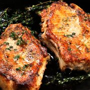 Juicy, browned pork steak on a bone in oil with garlic and herbs in a frying pan. Close-up.