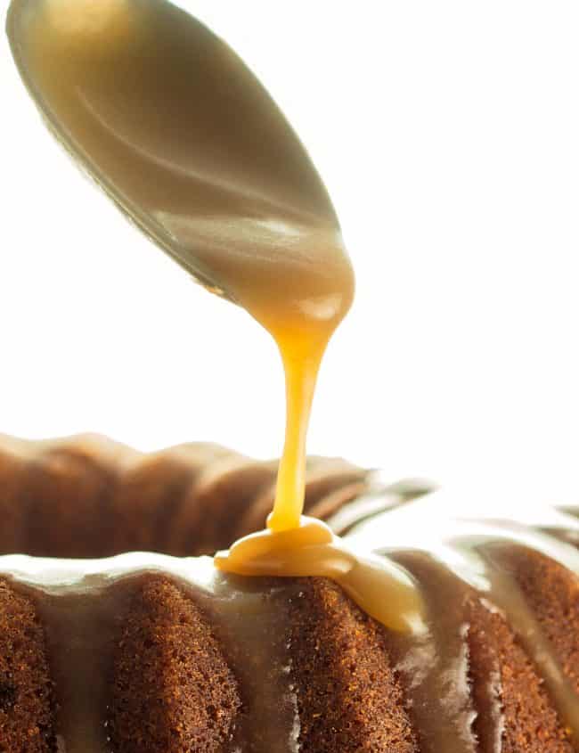a spoon adding caramel glaze to a cake