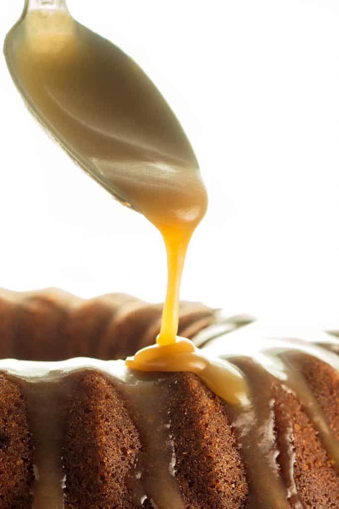 a spoon adding caramel glaze to a cake