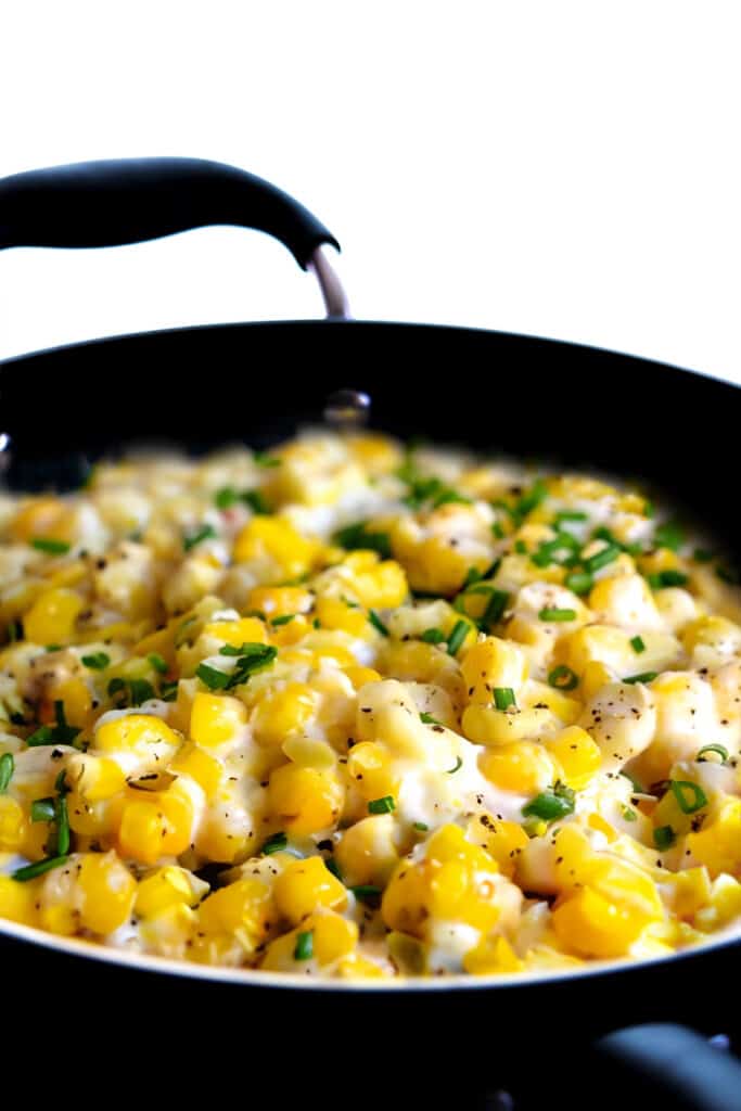 the finished dish of cream cheese corn scattered with chopped fresh herbs