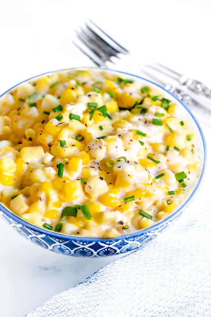 A bowl of corn in a cream sauce topped with fresh herbs