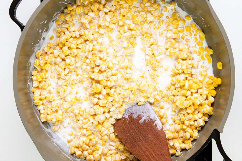 Corn kernels simmer gently in a creamy, savory mixture enhanced with cream cheese, stirred smoothly with a wooden spatula for a luxurious Cream Cheese Corn experience.