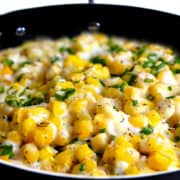 a close up image of cream cheese corn scattered with chopped fresh herbs.