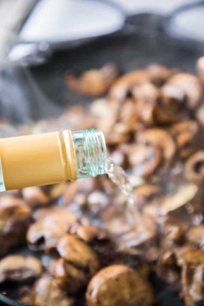 wine being poured into mushrooms in a pan