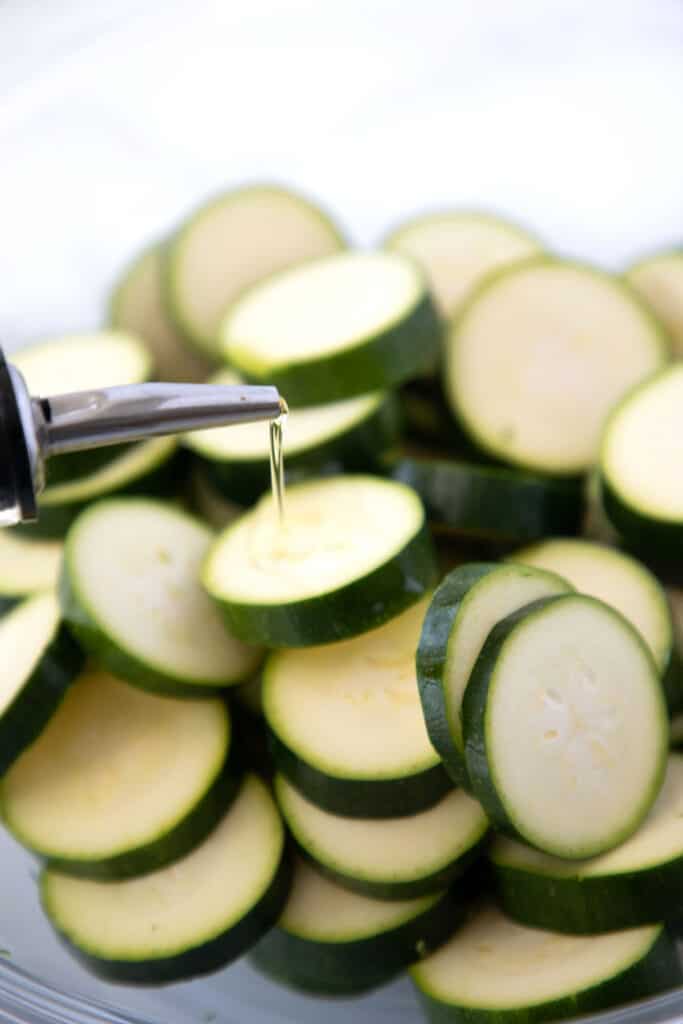 oil being poured onto sliced zucchini