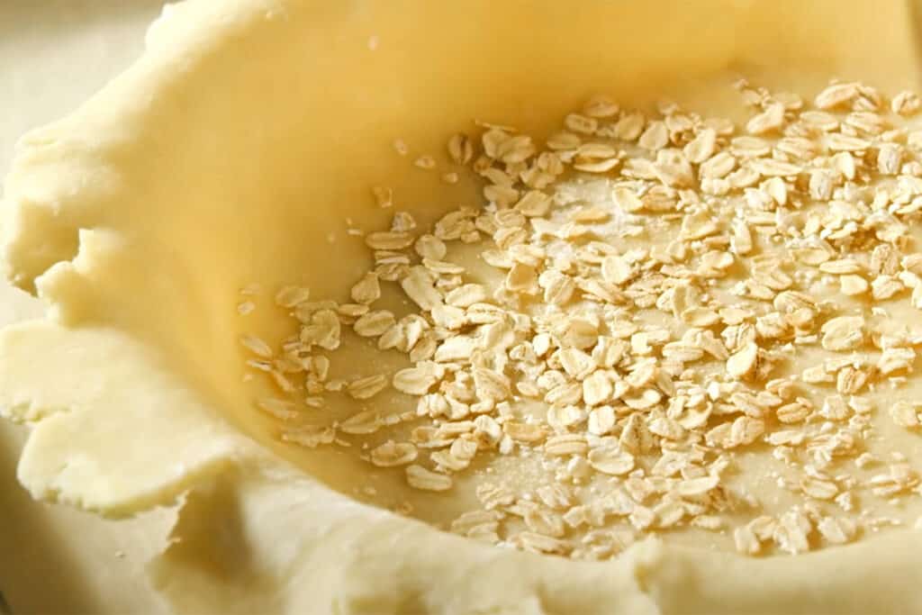 oats in the bottom of a pie dish lined with raw dough