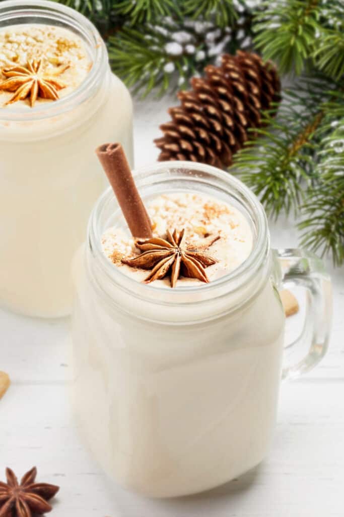 A glass mug filled with homemade eggnog garnished with star anise and a cinnamon stick