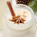 a mug of fresh eggnog garnished with star anise and a cinnamon stick with Christmas garland in the background