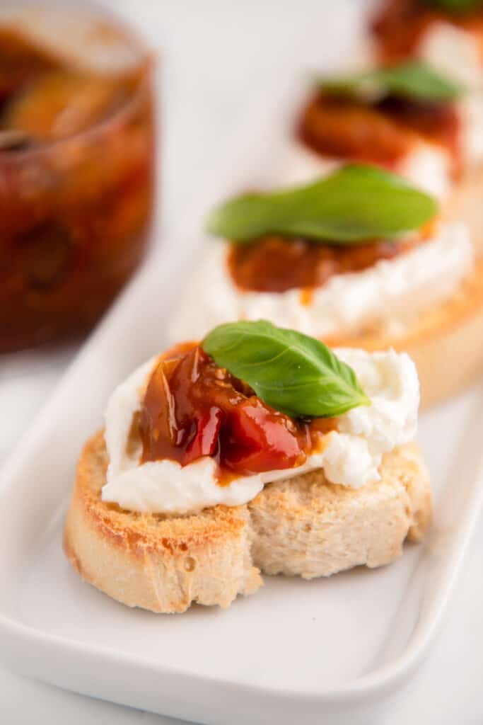 a tray of crostini bruschetta with tomato jam and a basil garnish