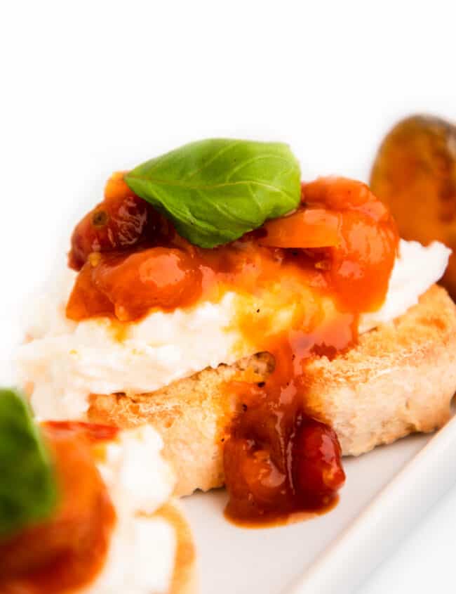 Crostini with burrata cheese, tomato jam and a basil garnish