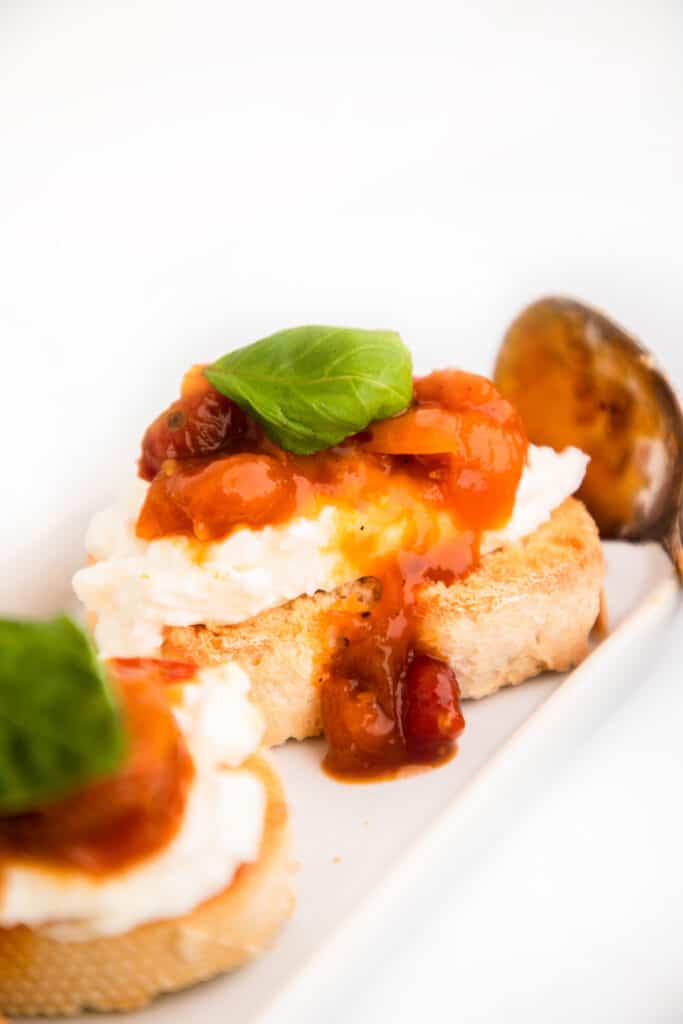 Crostini with burrata cheese, savory tomato jam and a basil garnish