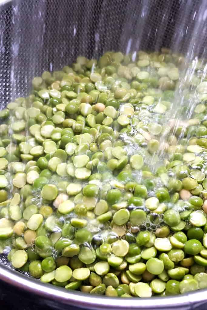 a strainer with split peas being rinsed under water