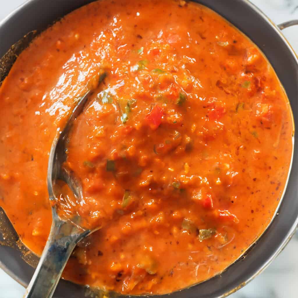 The peri peri chicken sauce cooked in a pot with a spoonful over the pot.