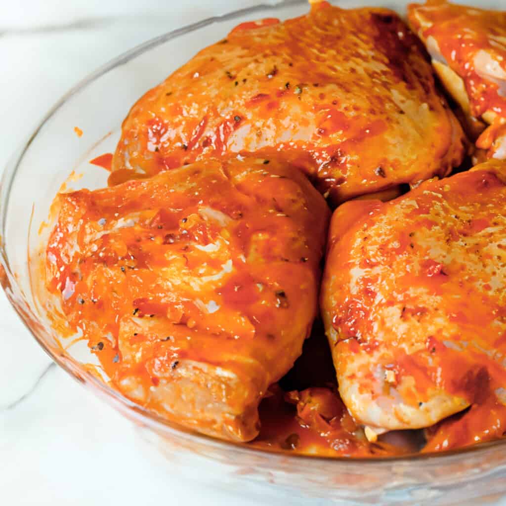 the chicken thighs coated in the peri peri marinade in a glass bowl.