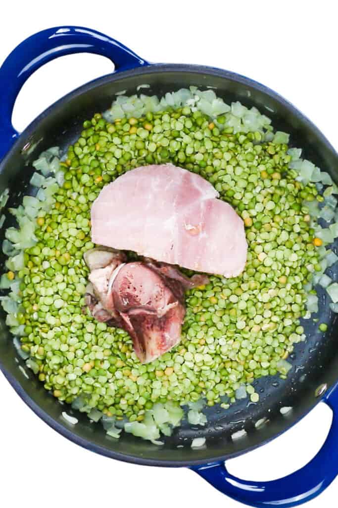 The ham bone and cut of ham added to the pan with the slit pea mixture