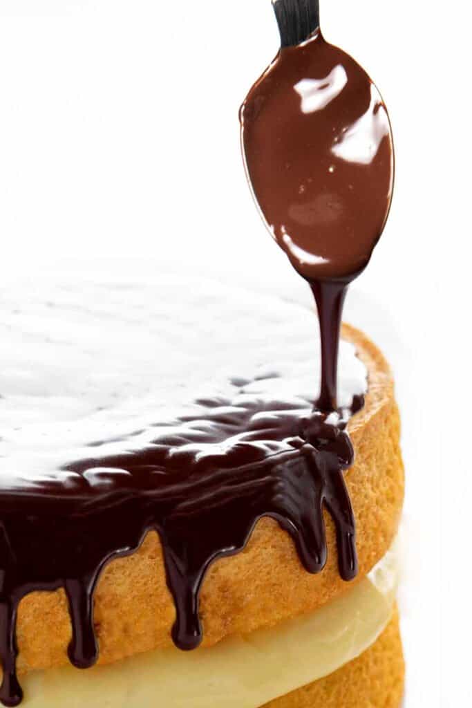 Chocolate glaze being spooned onto a custard filledcake