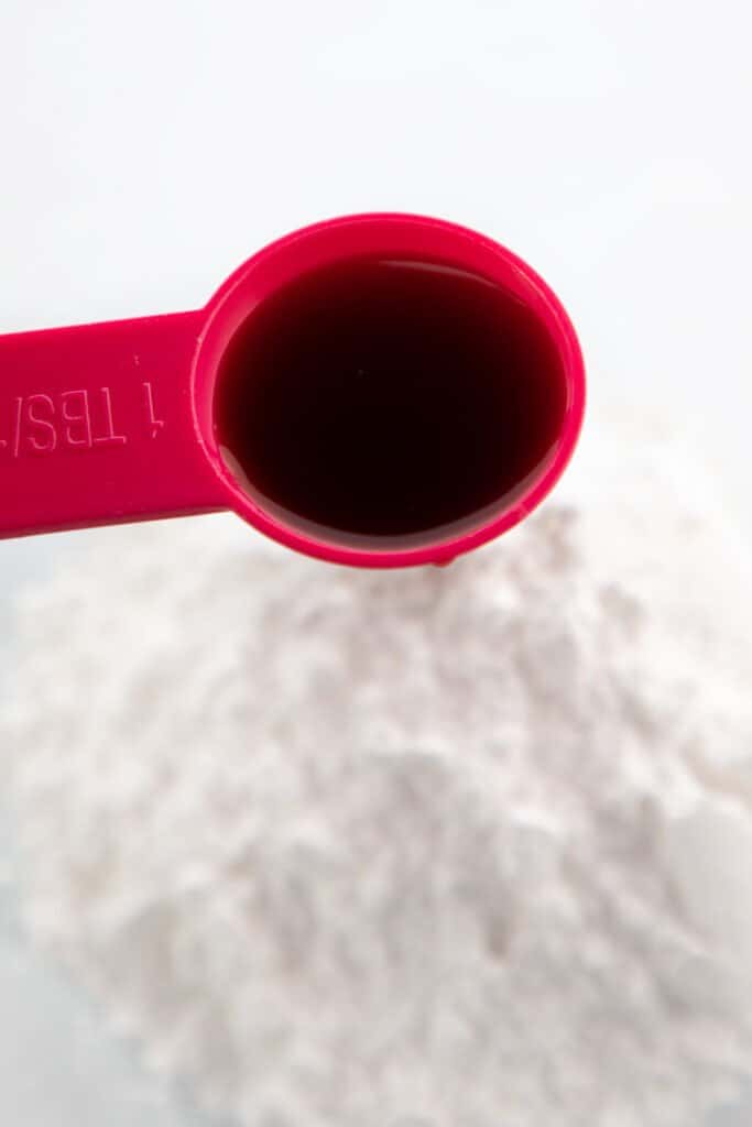 a spoon of vanilla over a mixing bowl with powdered sugar in it.