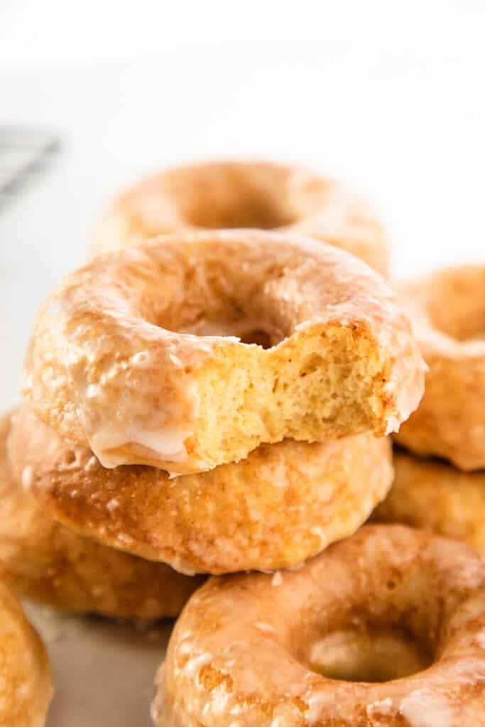 a pile of glazed donuts with the top one missing a bite