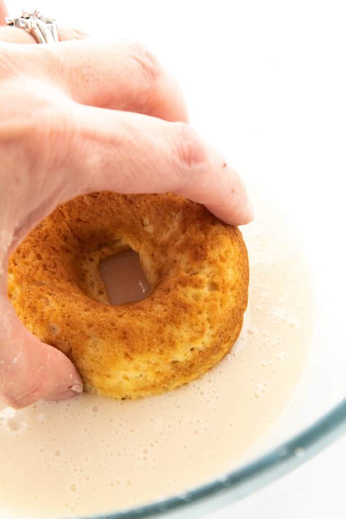 a donut being dipped into glaze in a bowl