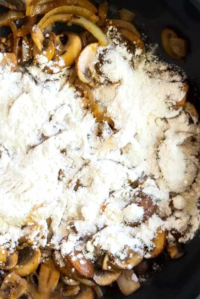 flour sprinkled on top of mushrooms frying in a pan