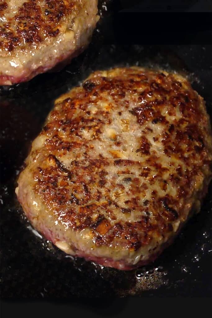 two beef steak patties in a pan