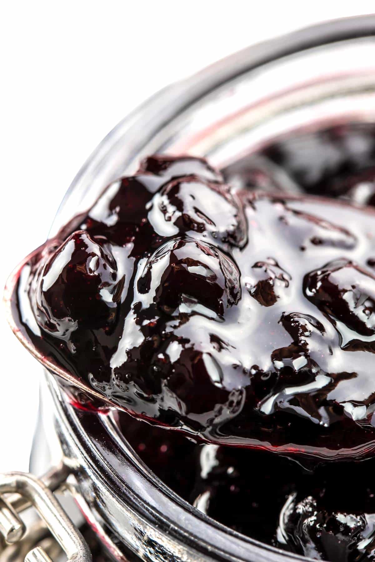 a close up of a spoonful of blueberry jam over a jar