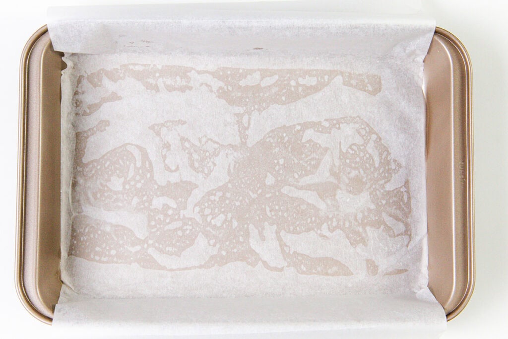 A rectangular baking tray lined with parchment paper, some areas wet or translucent—ready for baking the Best Lemon Squares Recipe.