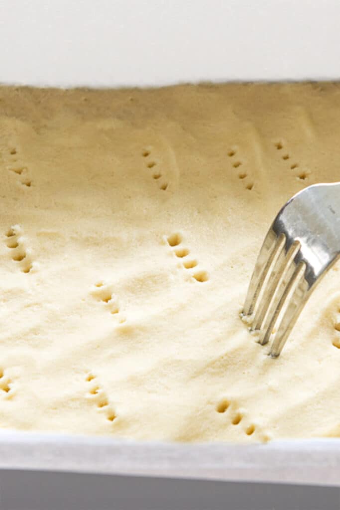 a fork pricking shortbread dough in a pan