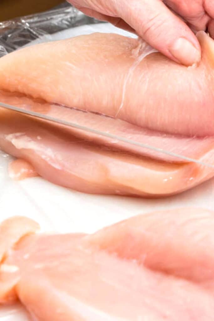 a chicken breast being sliced with a knife
