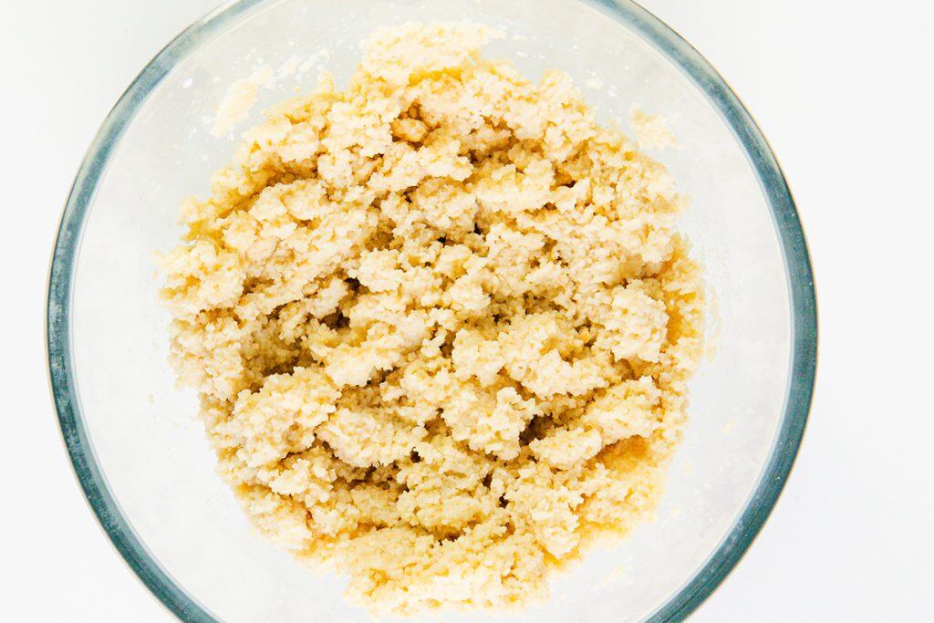 A glass bowl filled with pale, crumbly Salisbury Steak mixture, viewed from above on a white surface.