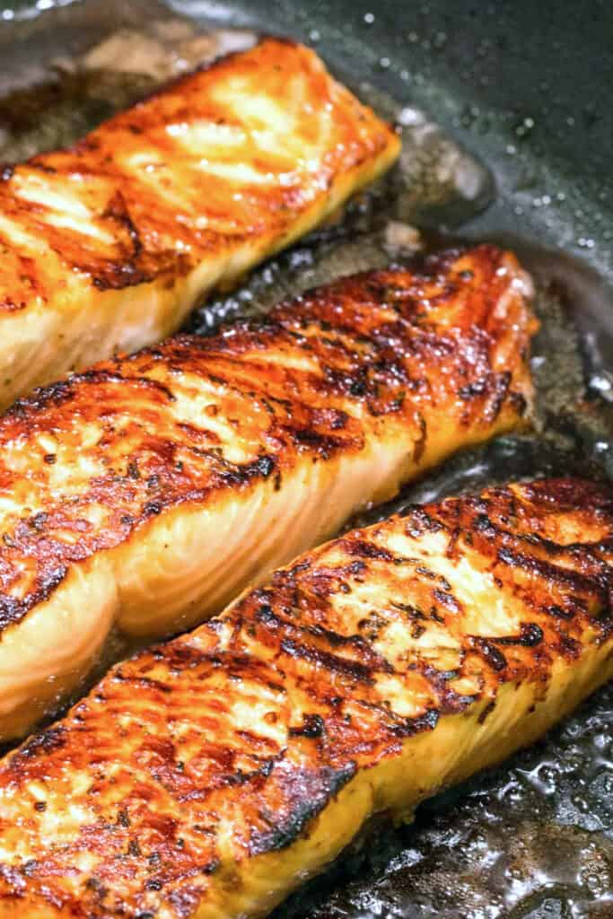 three crisp seared salmon fillets in a pan