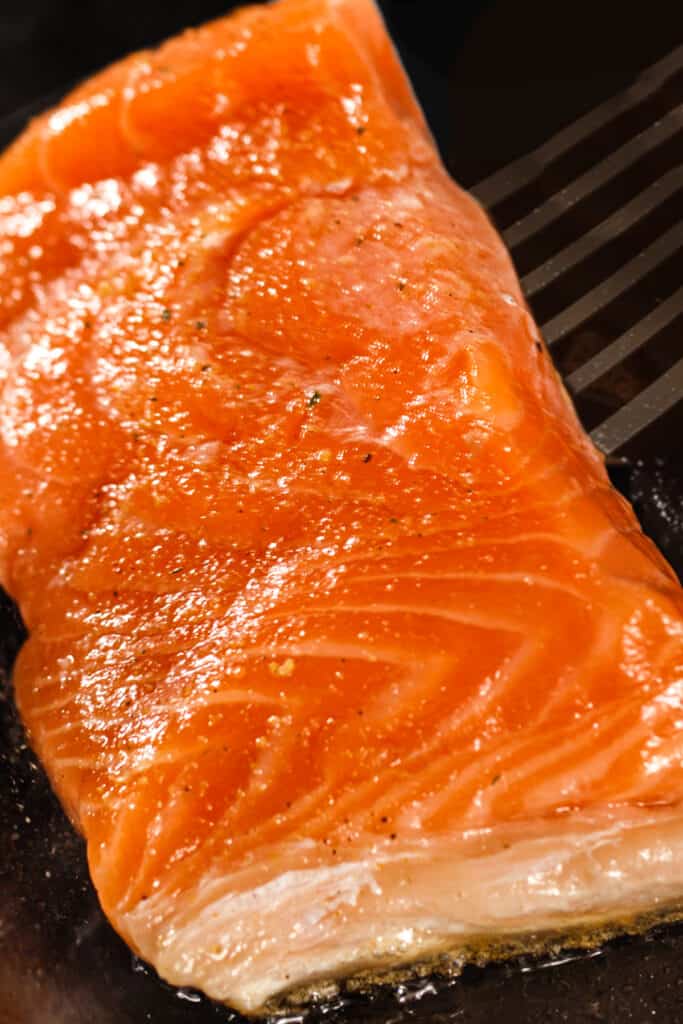 a salmon fillet being flipped in the pan