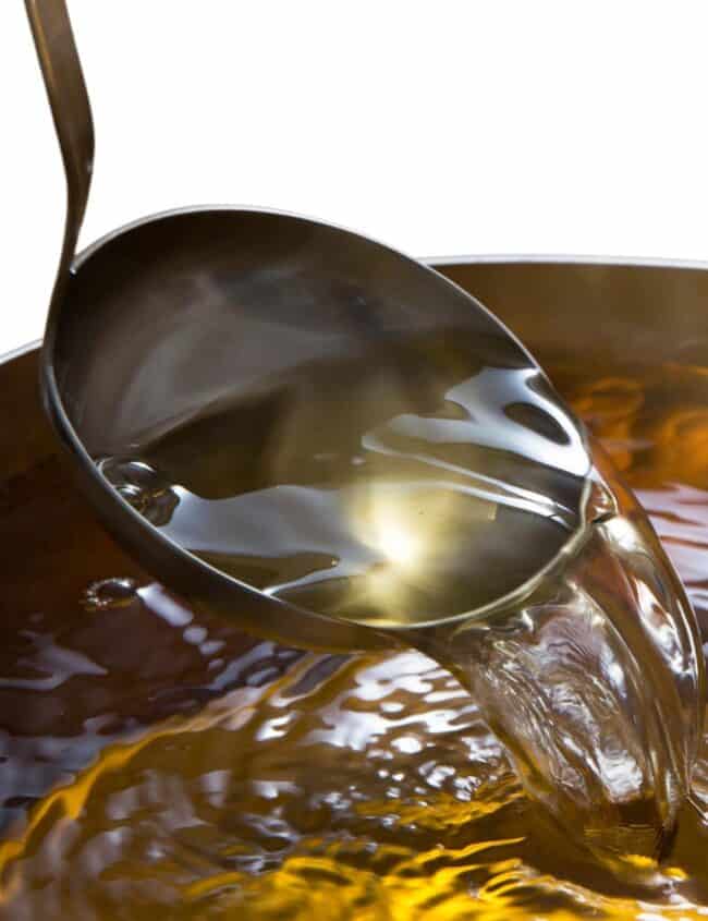 a ladle pouring stock into a pot