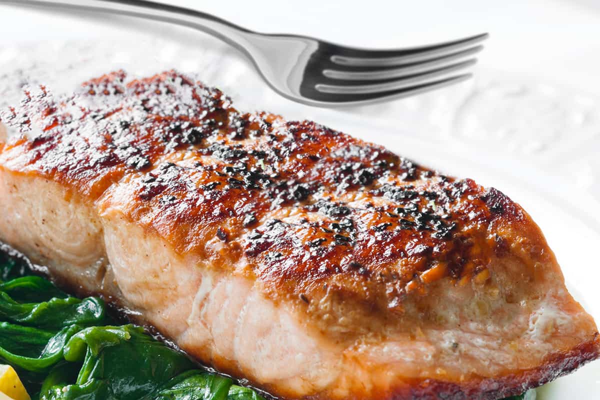 a crispy pan seared salmon fillet on a bed of spinach and a fork in the background