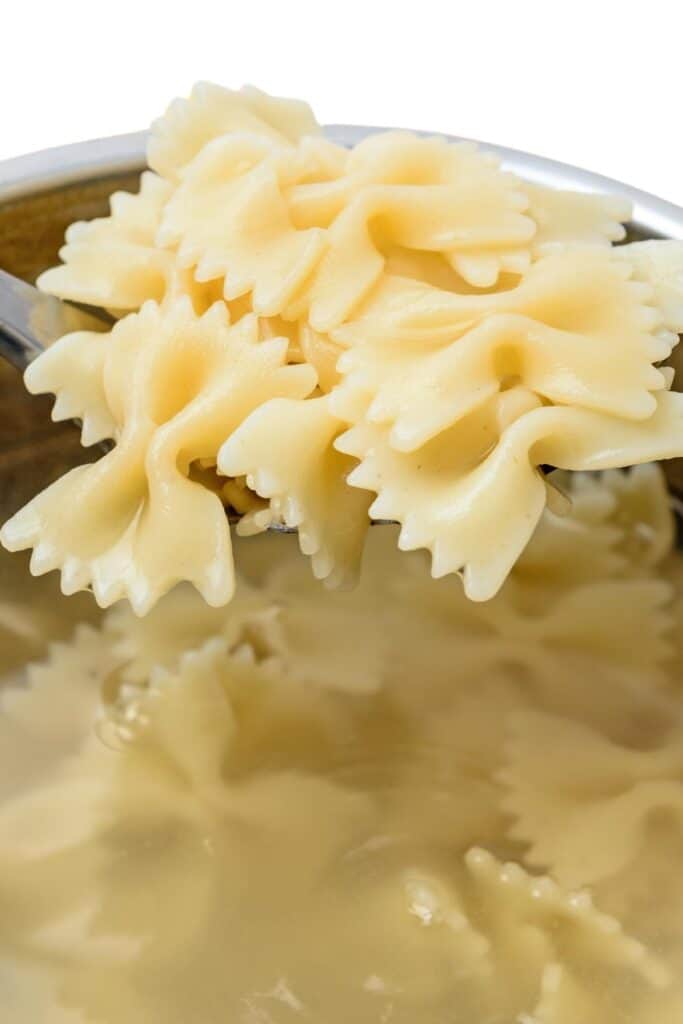 a spoon of bow tie pasta over a bot of cooking pasta