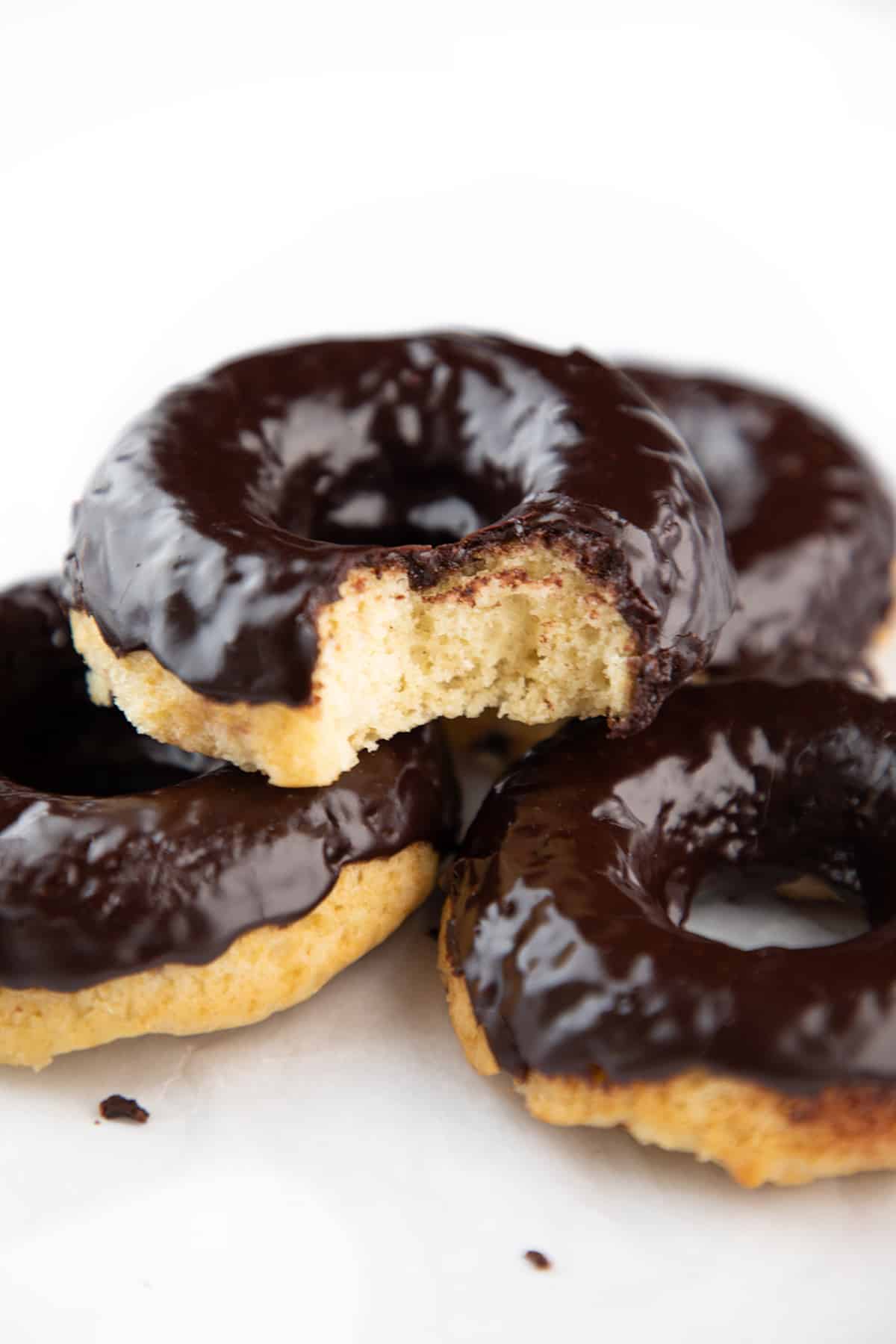 a pile of Chocolate frosted donuts with the top one missing a bite