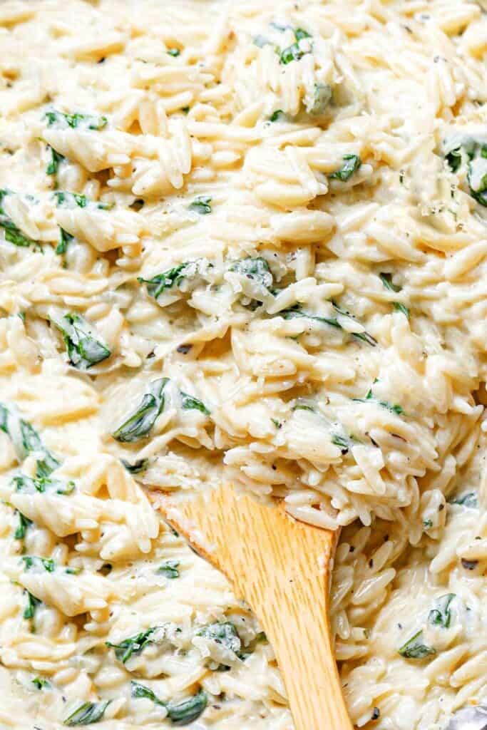 a close up of creamy orzo and spinach with a wooden spoon