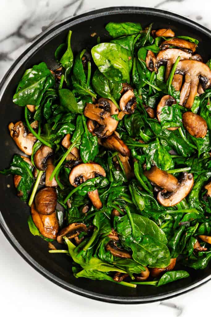 cooked mushrooms and spinach cooked in a skillet.
