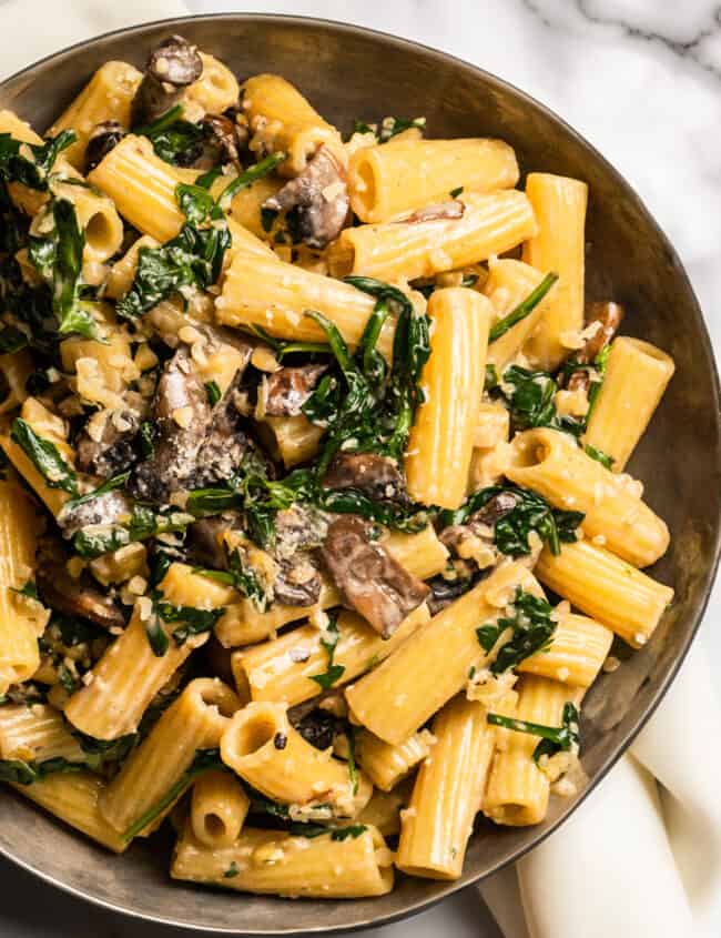 Freshly Cooked Creamy Parmesan Spinach Mushroom Pasta in a bowl with a white cloth napkin.