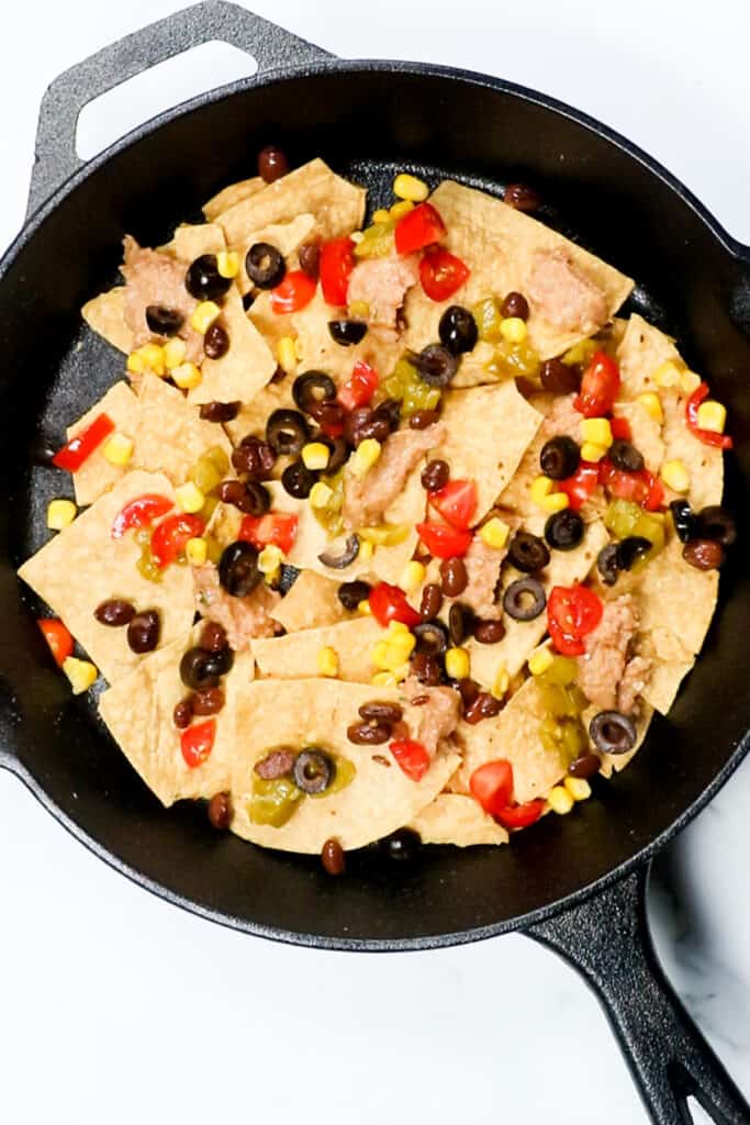 tortilla chips in a single layer in a skillet topped with nacho toppongs