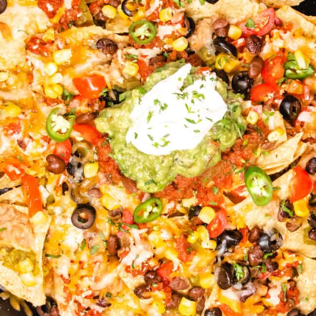 a close up image of a cast iron pan with nachos topped with guacamole and sour cream