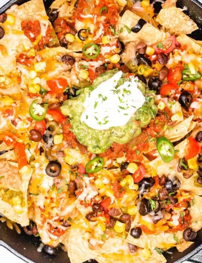 a close up image of a cast iron pan with nachos topped with guacamole and sour cream