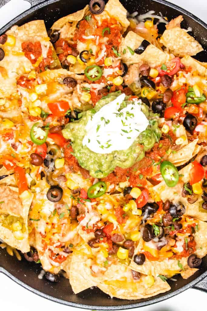 a close up image of a cast iron pan with nachos topped with guacamole and sour cream