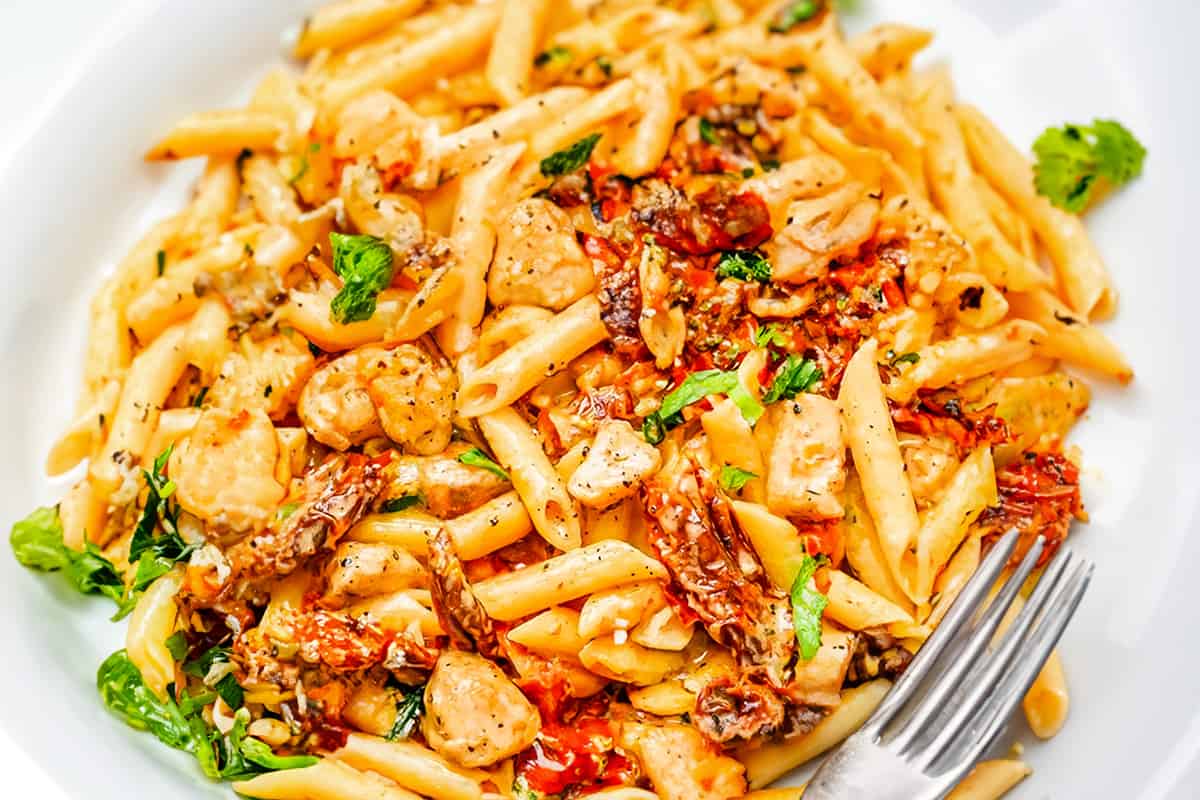 a white plate with Chicken Sundried Tomato Pasta and a fork.