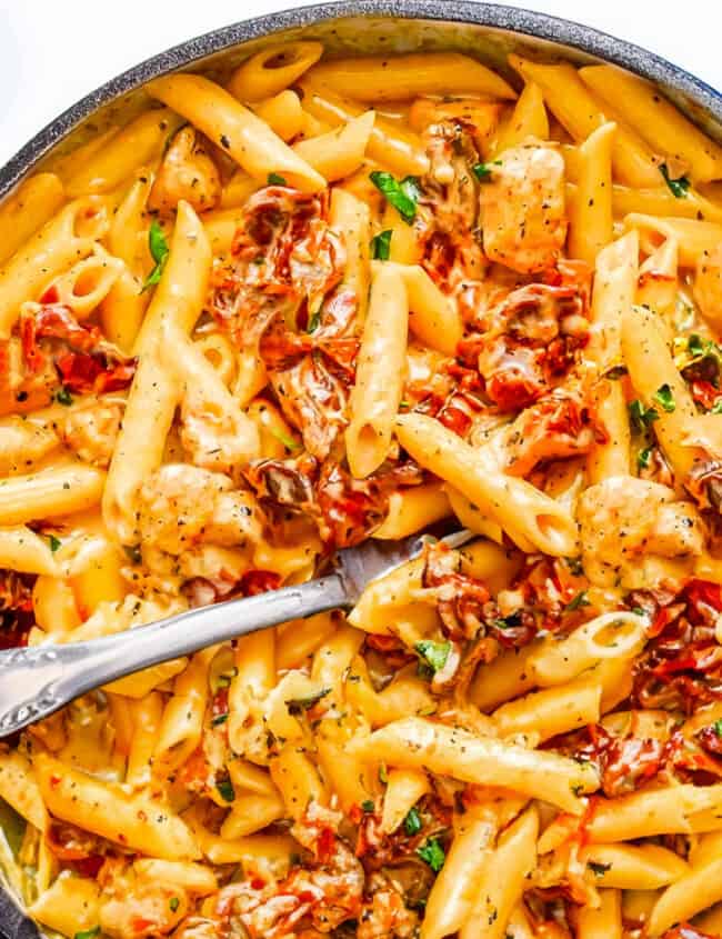 a pot of creamy Sun-Dried Tomato Pasta with chunks of chicken and sundried tomatoes.