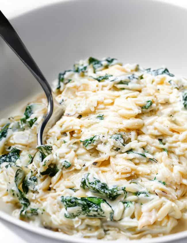 a bowl of creamy orzo with spinach and a spoon in the bowl