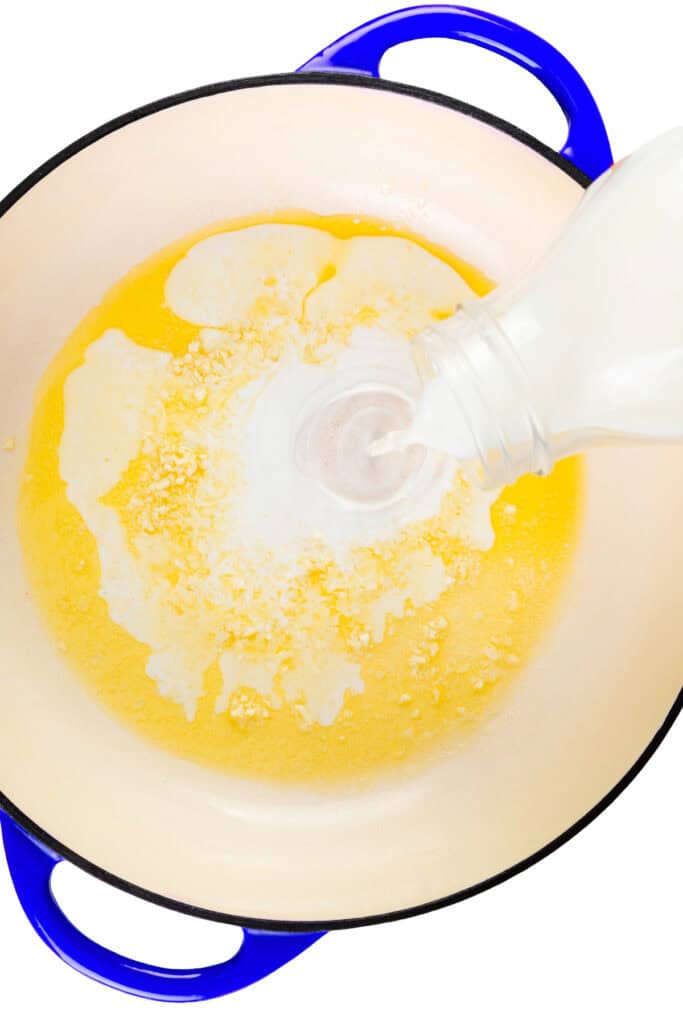 Milk is being poured from a bottle into a pot containing melted butter and minced garlic to start the base for Parmesan Lemon Orzo Pasta, with a blue handle visible on the side of the pot.