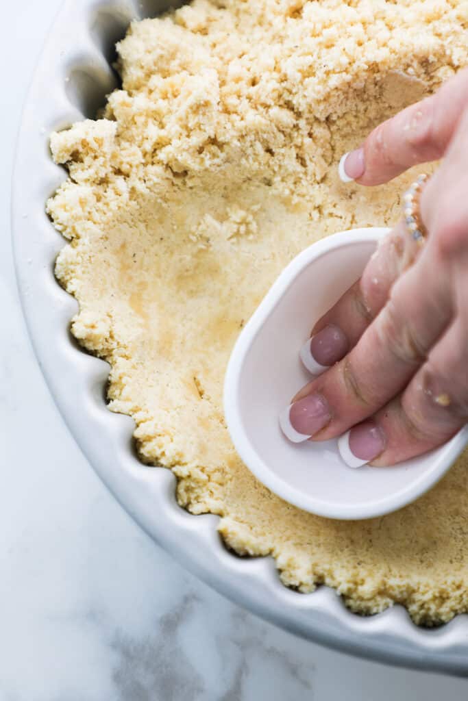 a cup pushing the dough for the Shortbread Crust {Sablé Breton} into the pan