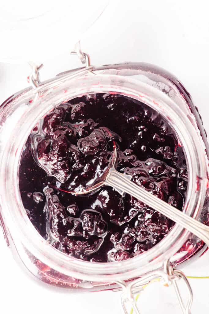 a close up image of a spoonful of Cherry Jam Preserves over a jar